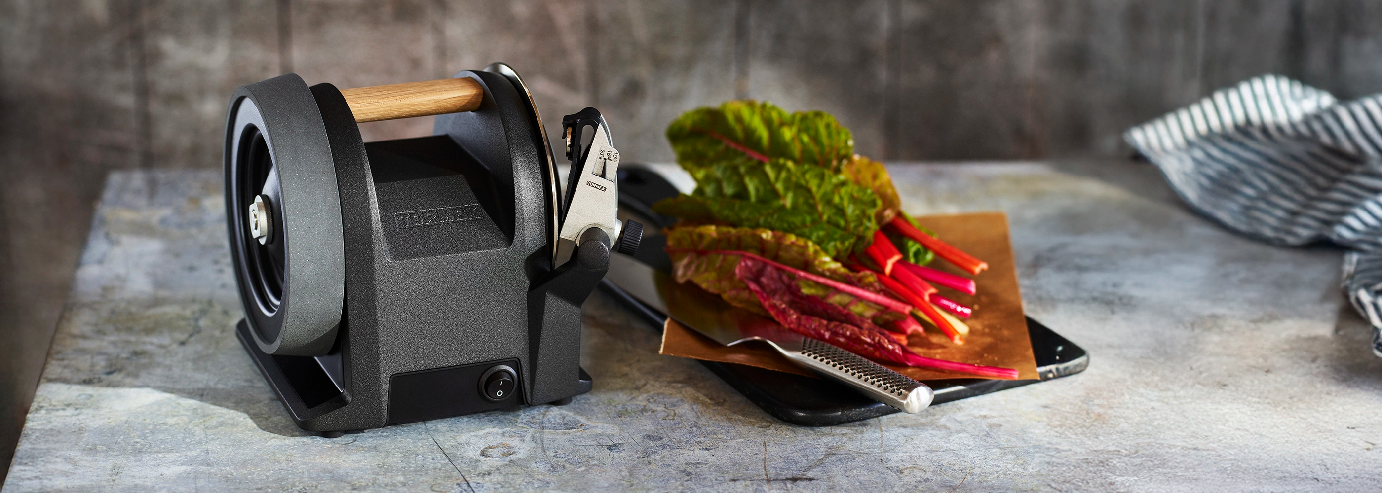 A Tormek T-1 Kitchen Knife Sharpener on a kitchen counter next to a chopping board filled with swiss chard.