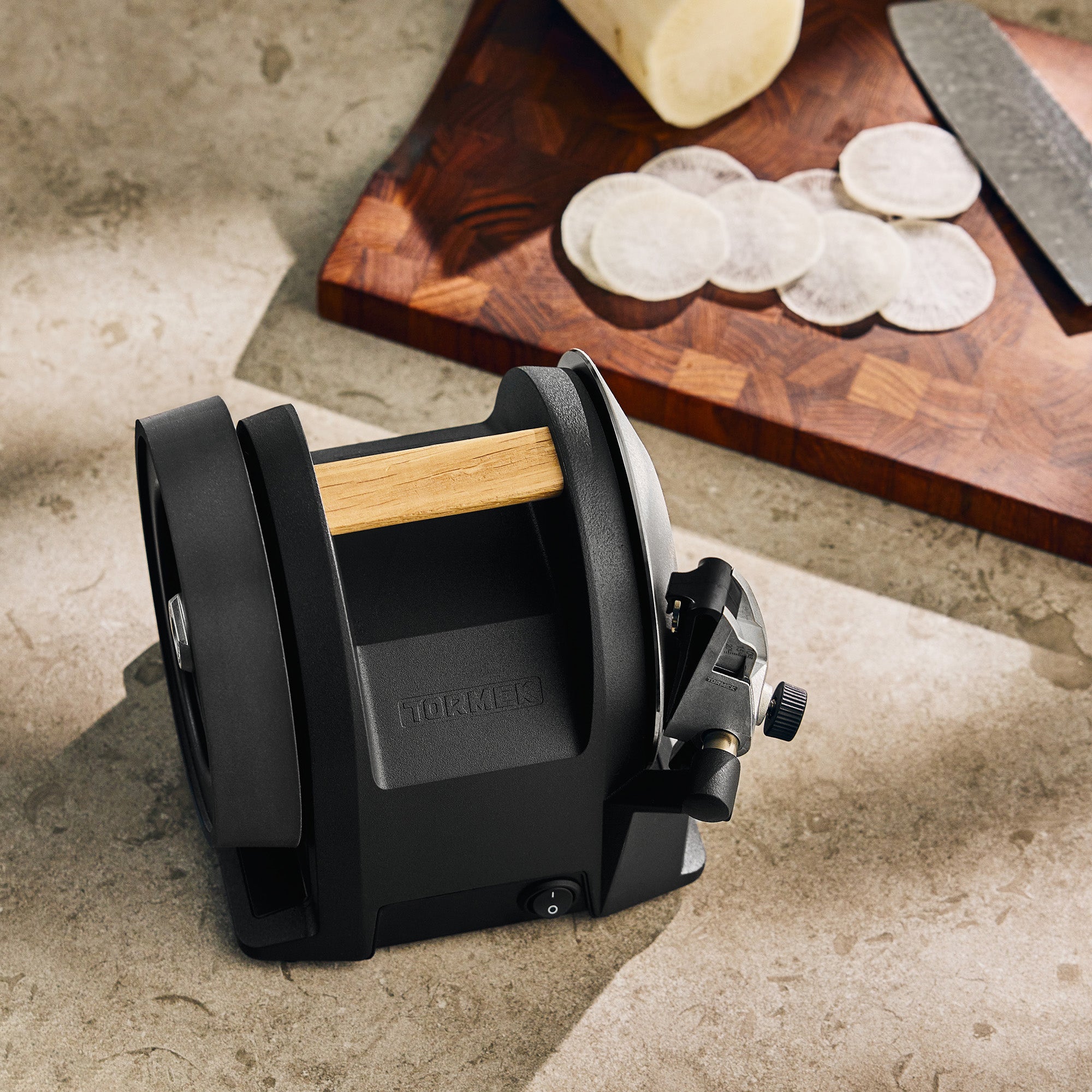 A Tormek T-1 Carbon Black on a stone counter before a cutting board with radish on it.