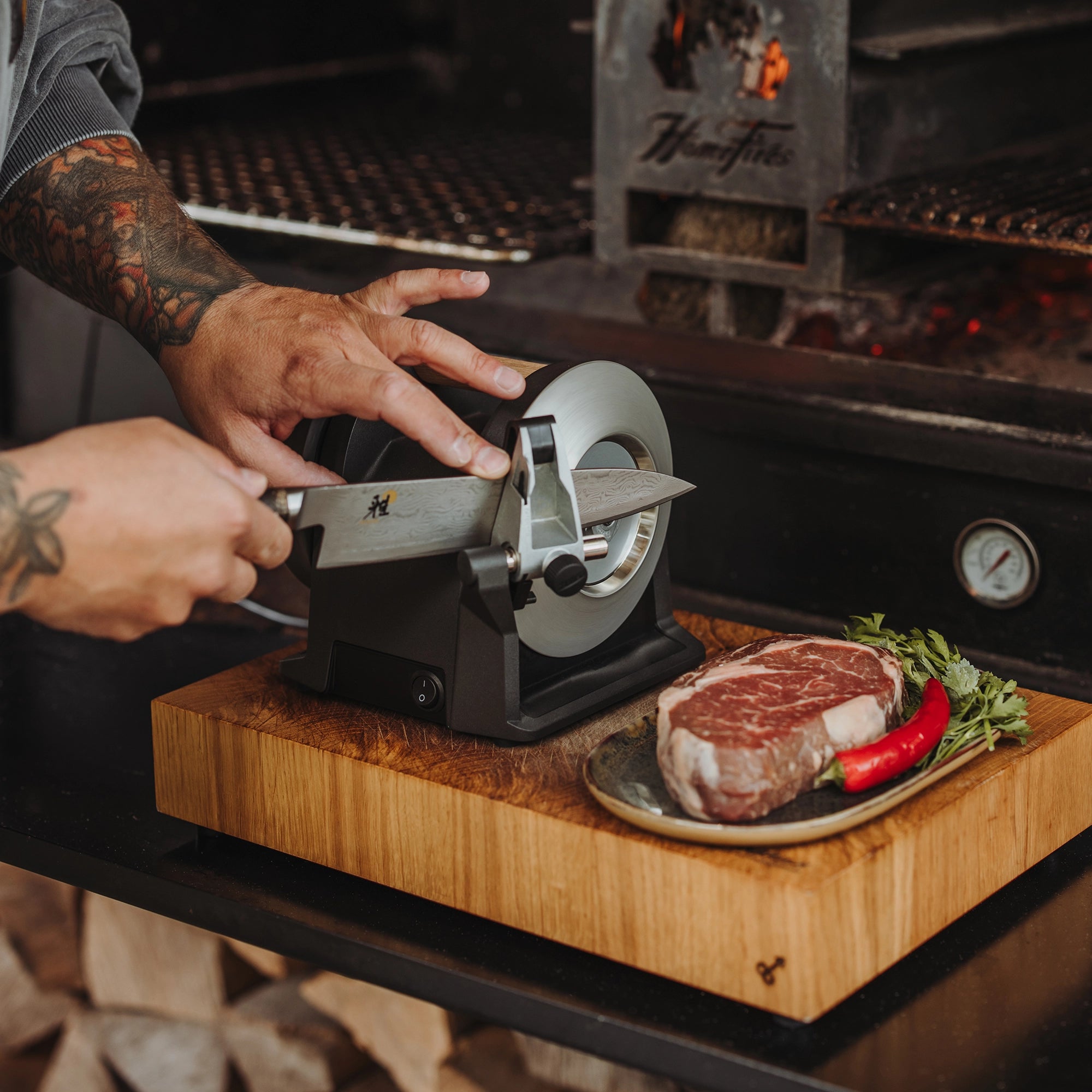 A knife is being sharpened on the T-1 Carbon Black next to a grill.