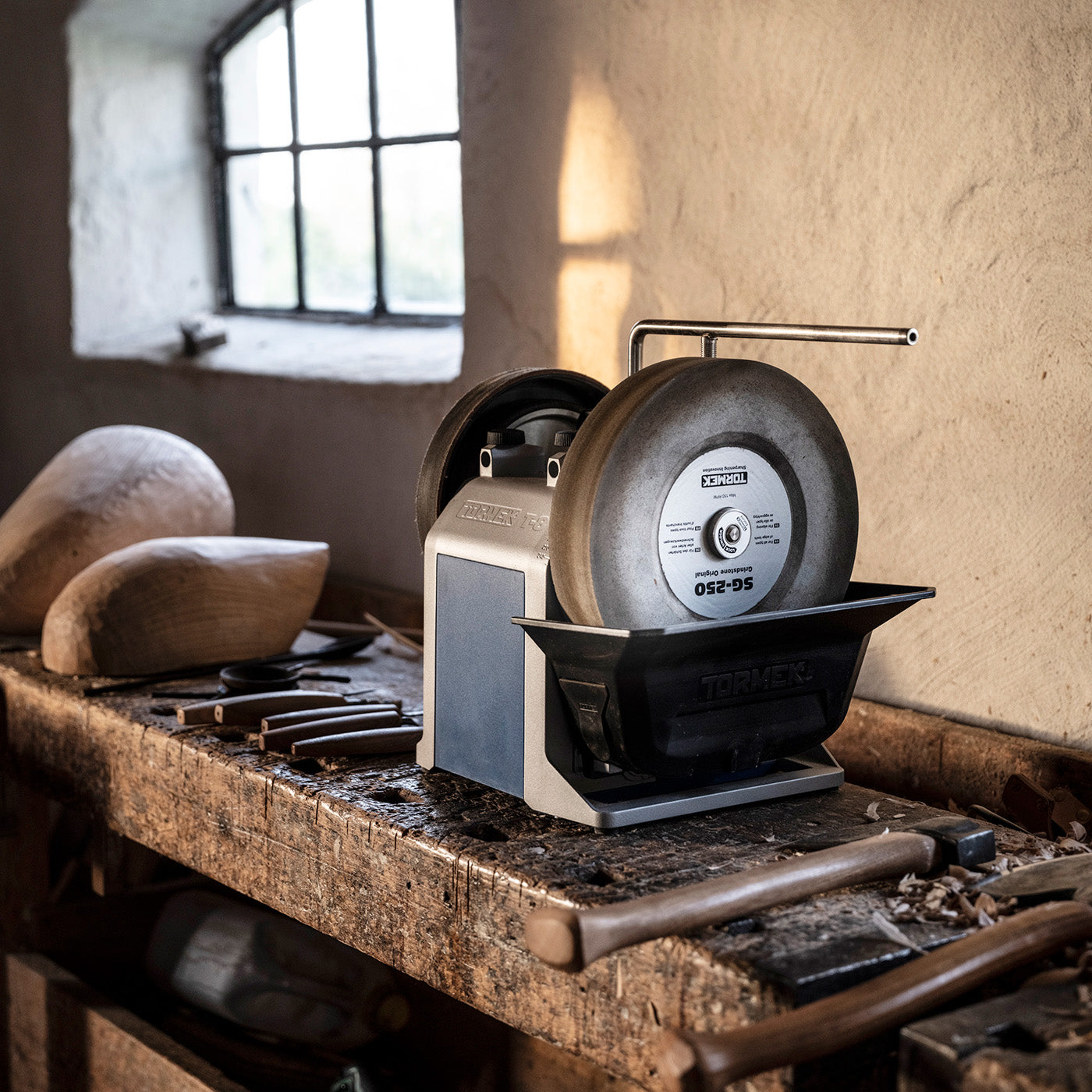 The Tormek T-8 standing in a woodworking studio surrounded by tools.